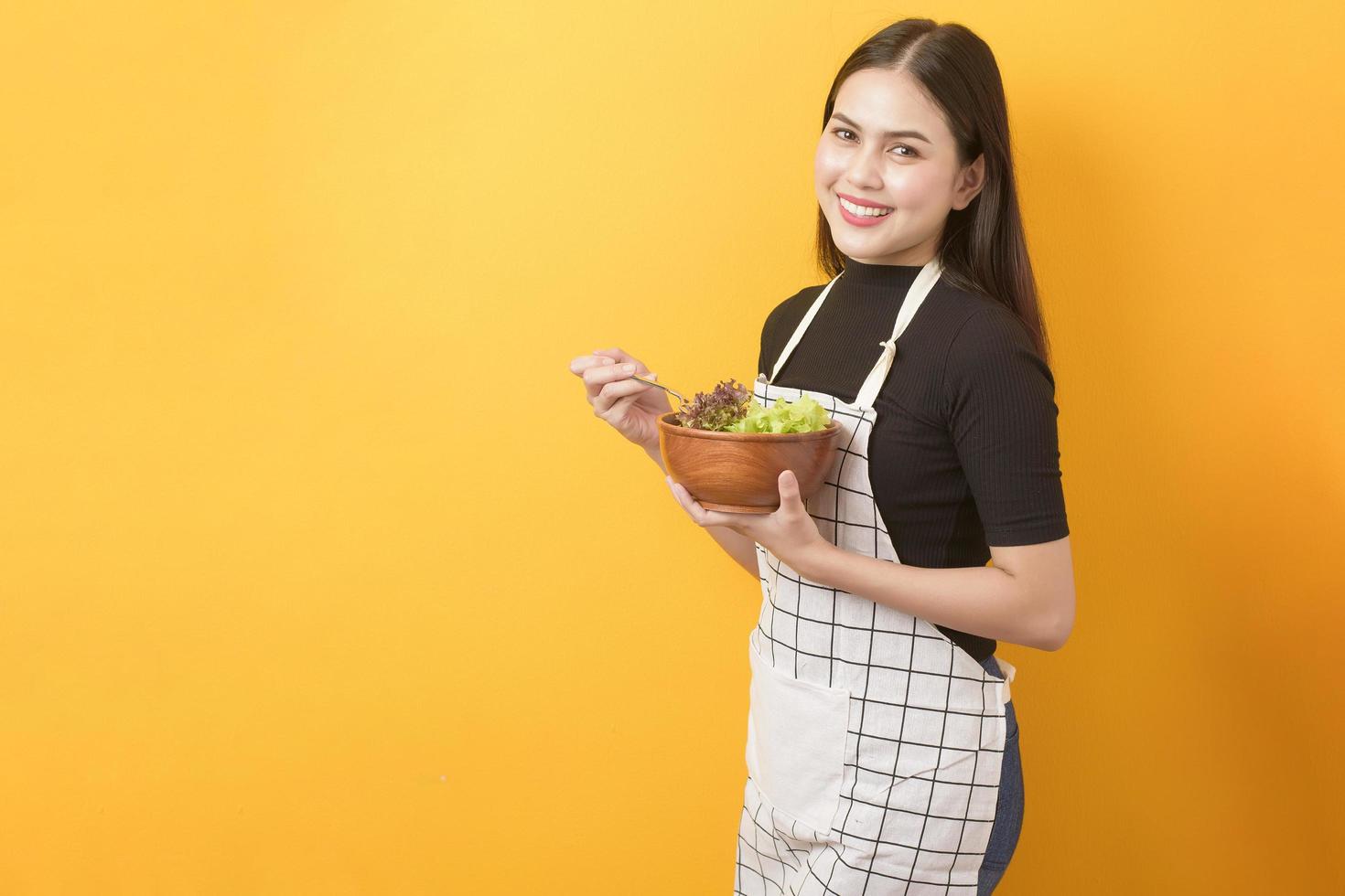 mooie gezonde vrouw eet groenten op gele achtergrond foto