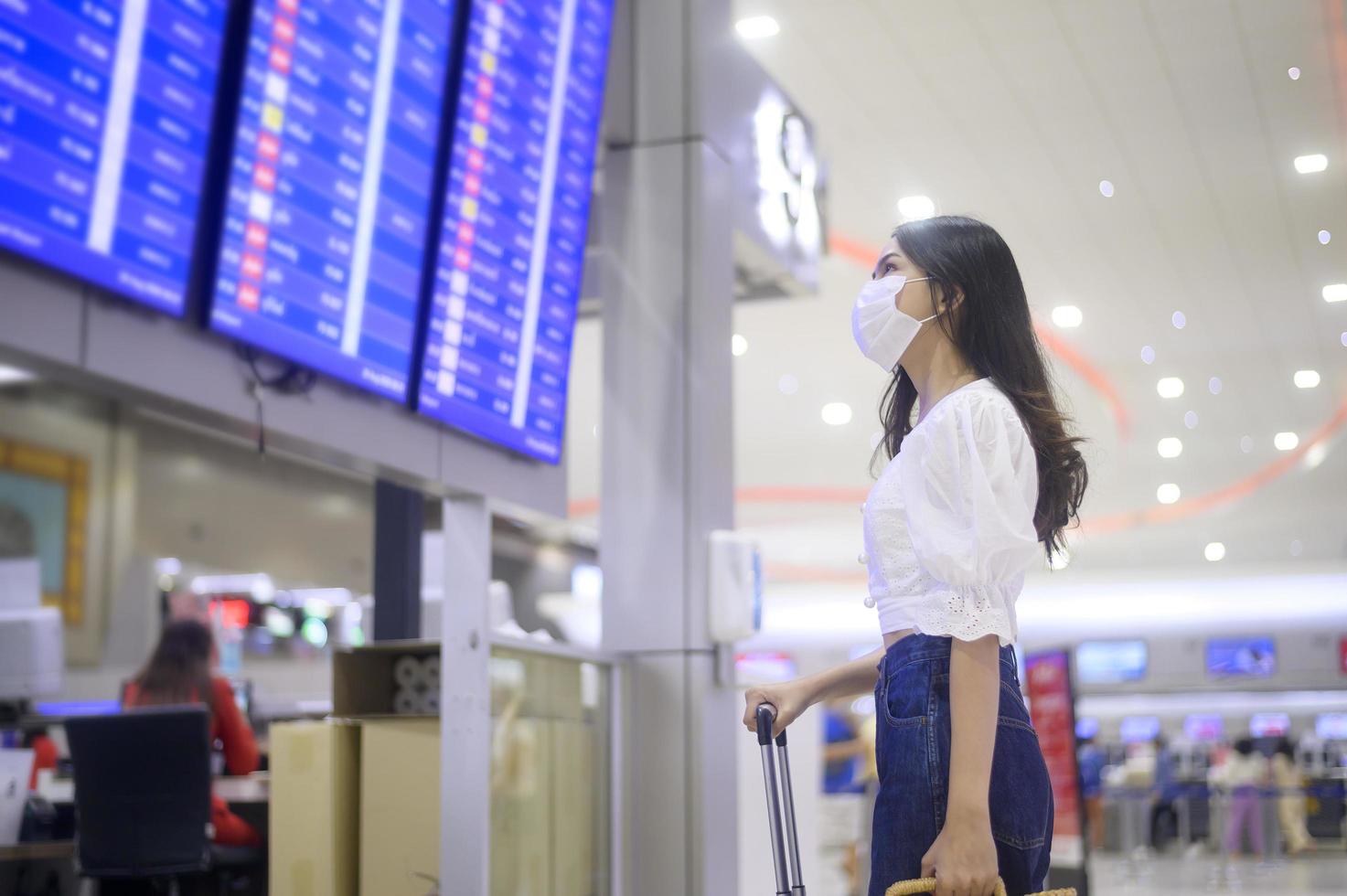 een reizigersvrouw draagt een beschermend masker op de internationale luchthaven, reist onder covid-19 pandemie, veiligheidsreizen, protocol voor sociale afstand, nieuw normaal reisconcept foto