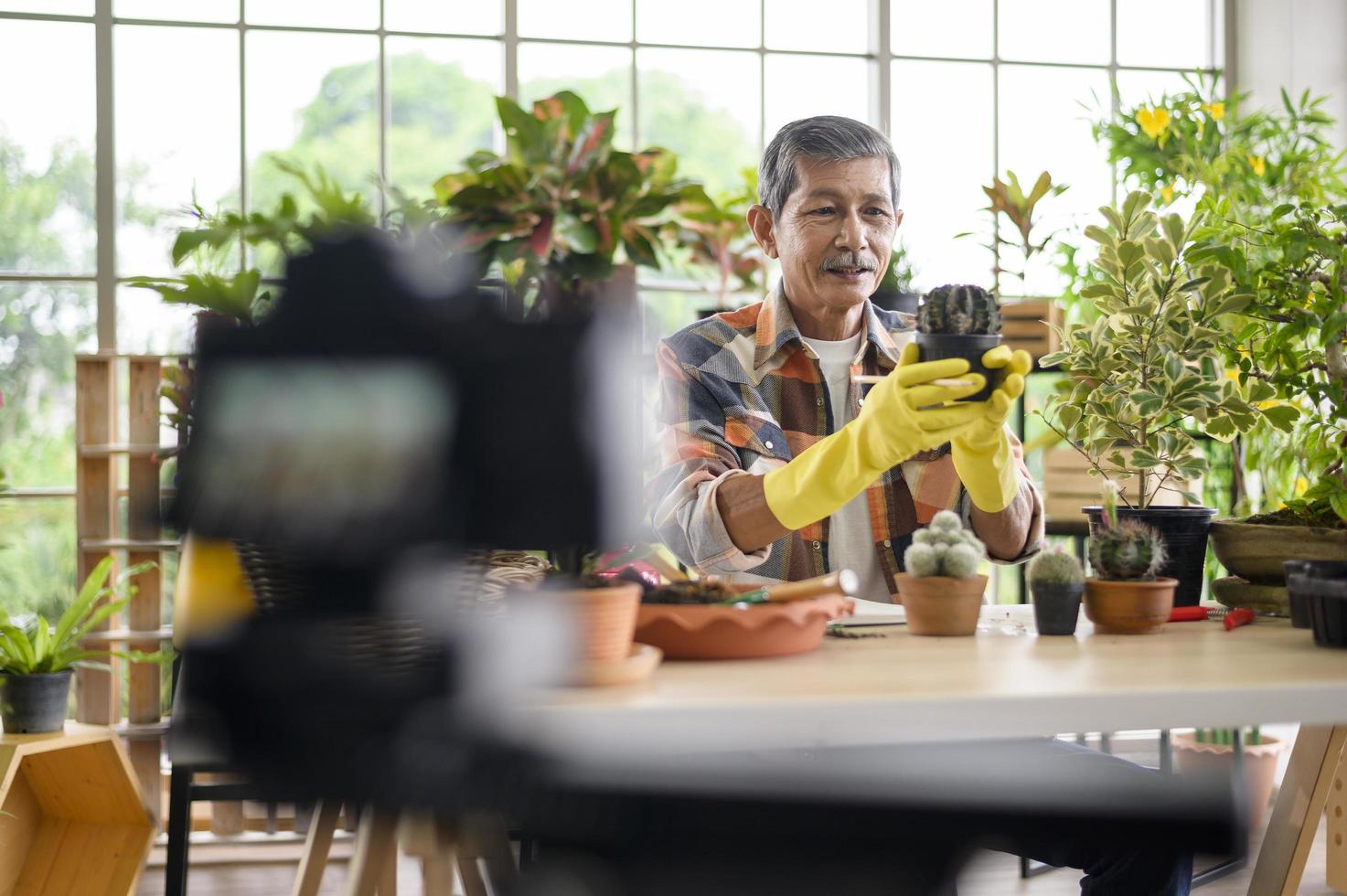 een senior man-ondernemer die met camera werkt, presenteert kamerplanten tijdens online livestream thuis en verkoopt online concept foto