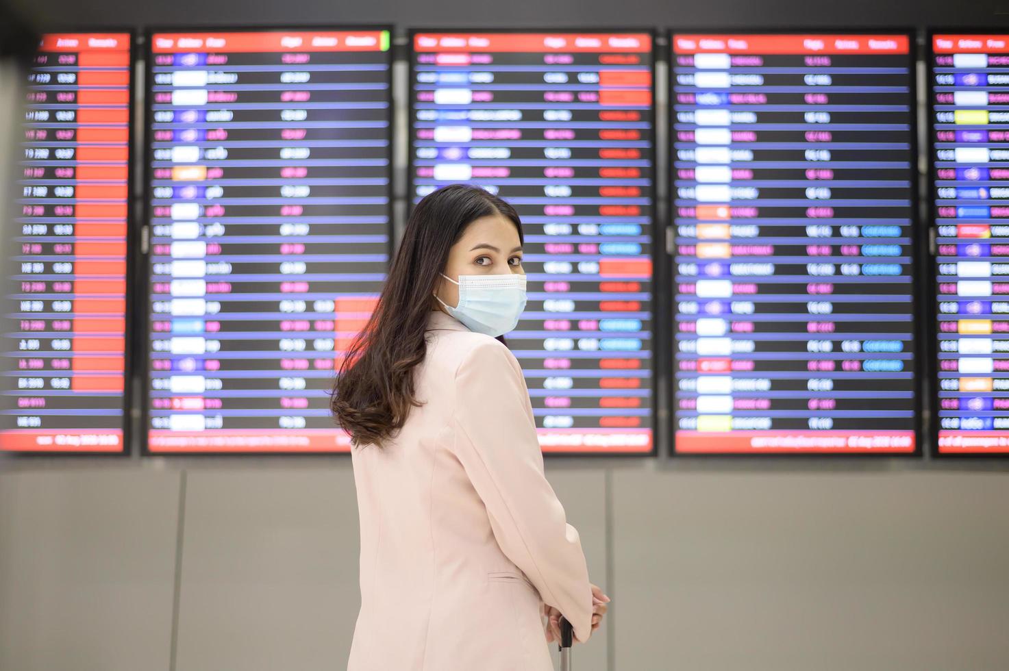 een zakenvrouw draagt een beschermend masker op de internationale luchthaven, reist onder covid-19 pandemie, veiligheidsreizen, protocol voor sociale afstand, nieuw normaal reisconcept foto