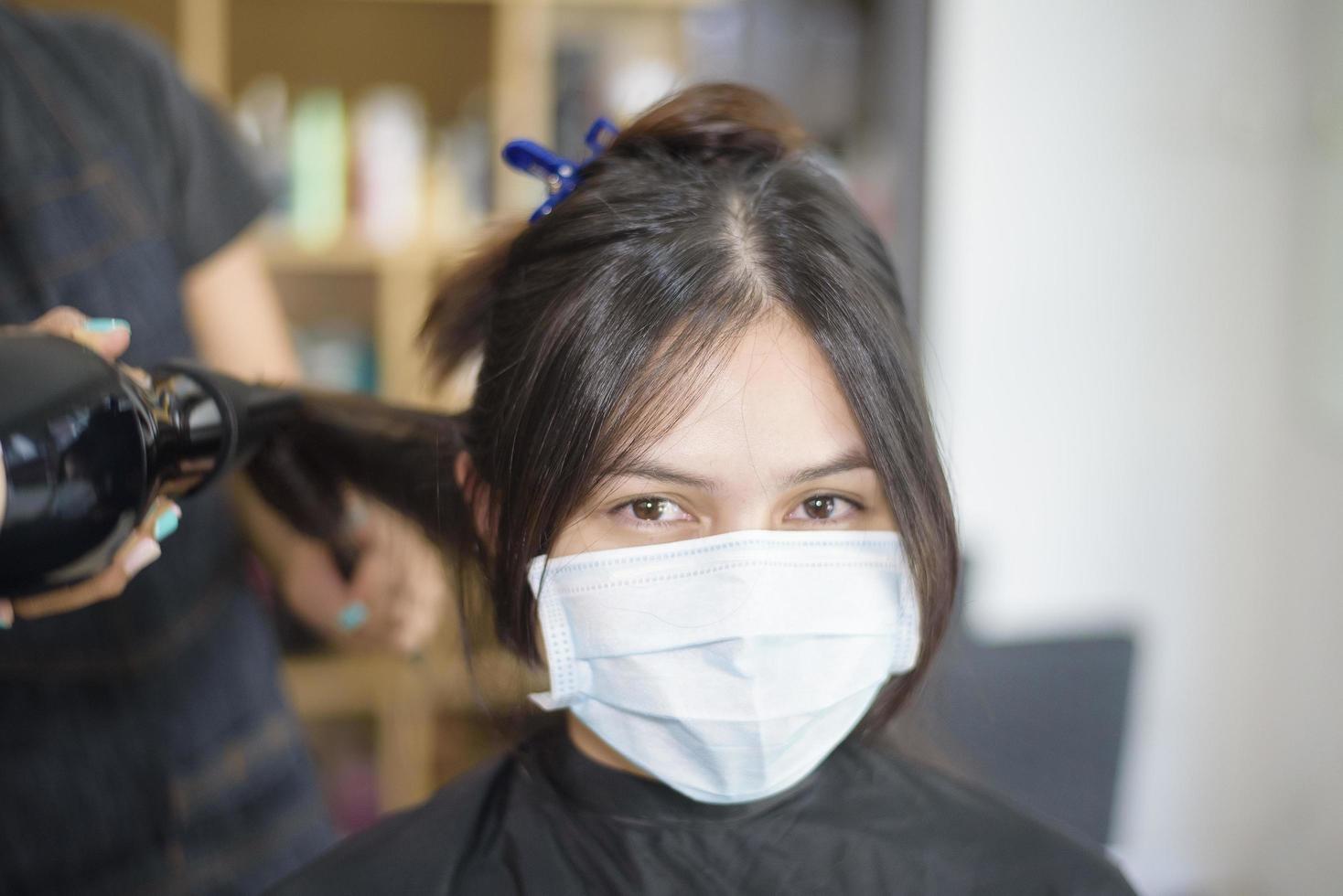 een jonge vrouw wordt geknipt in een kapsalon, draagt een gezichtsmasker voor bescherming covid-19, salonveiligheidsconcept foto