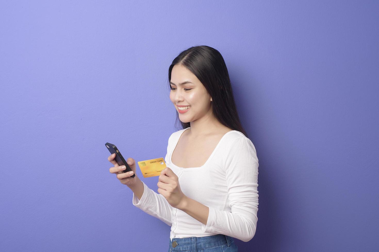 portret van jonge Aziatische vrouw gebruikt mobiele telefoon met creditcard op paarse achtergrond foto