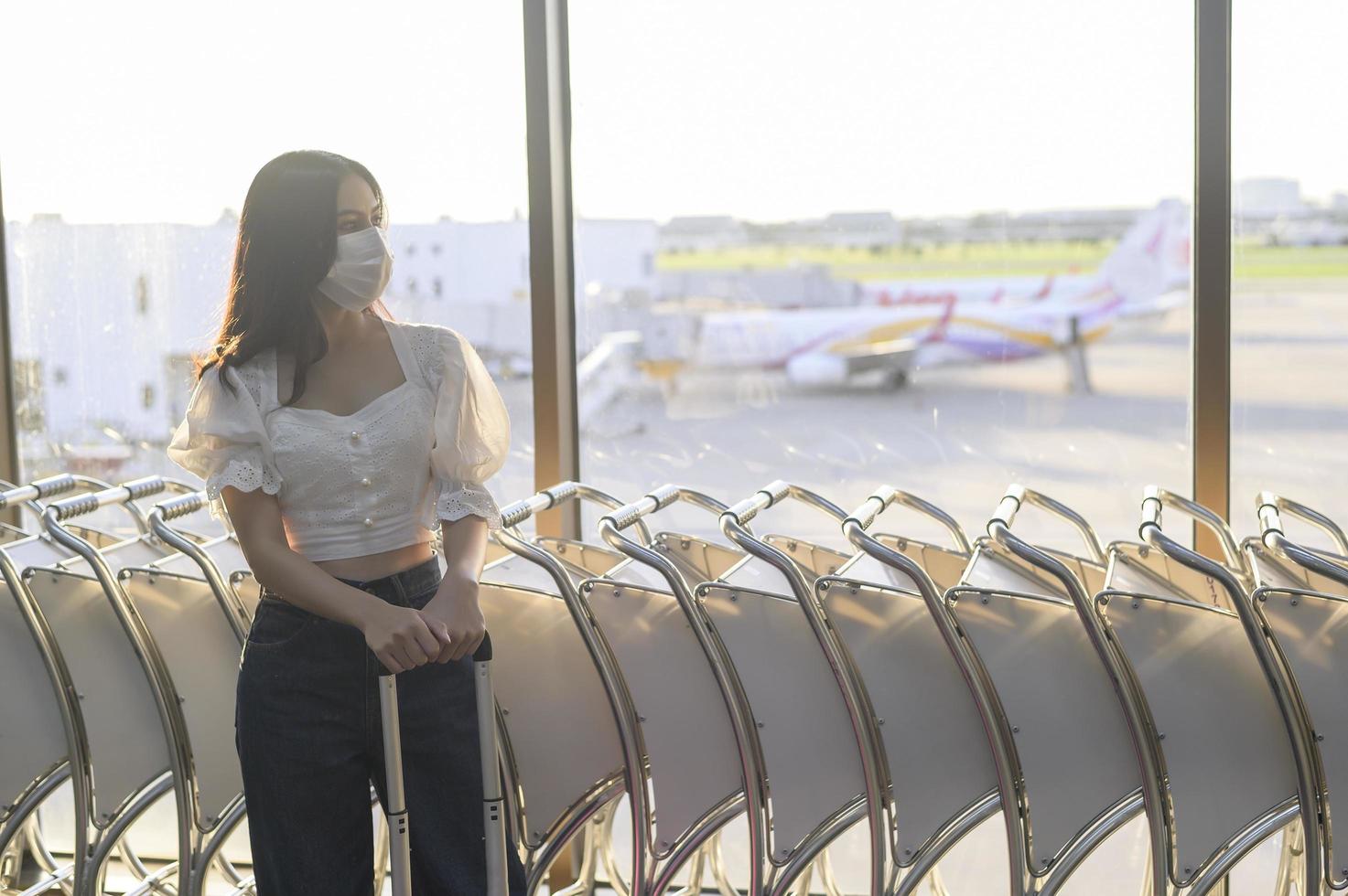 een reizigersvrouw draagt een beschermend masker op de internationale luchthaven, reist onder covid-19 pandemie, veiligheidsreizen, protocol voor sociale afstand, nieuw normaal reisconcept foto