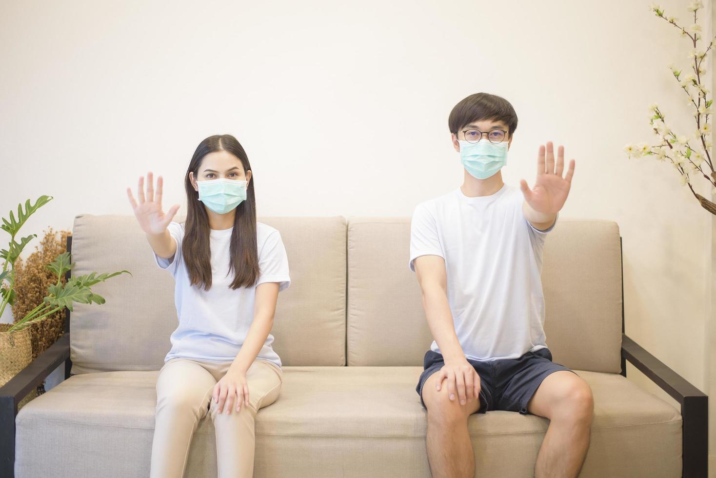 een stel dat een masker draagt, zit thuis op een bank tijdens quarantaine voor bescherming en ter voorkoming van coronavirus foto