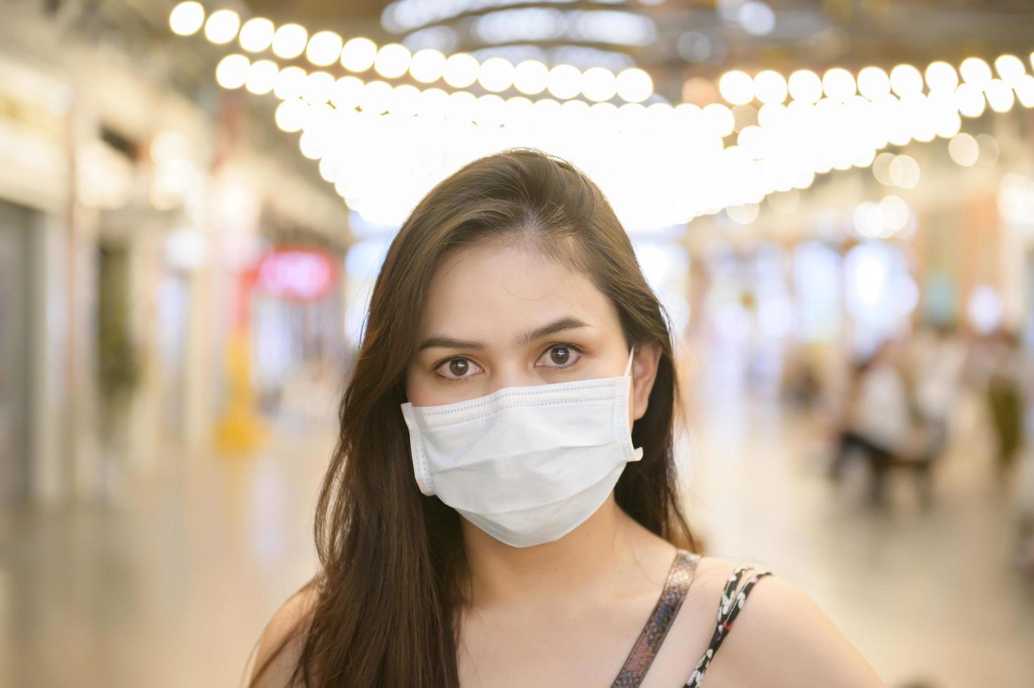 een jonge aziatische vrouw draagt een beschermend masker dat winkelt in het winkelcentrum, bescherming tegen het coronavirus, een nieuw normaal levensstijlconcept foto