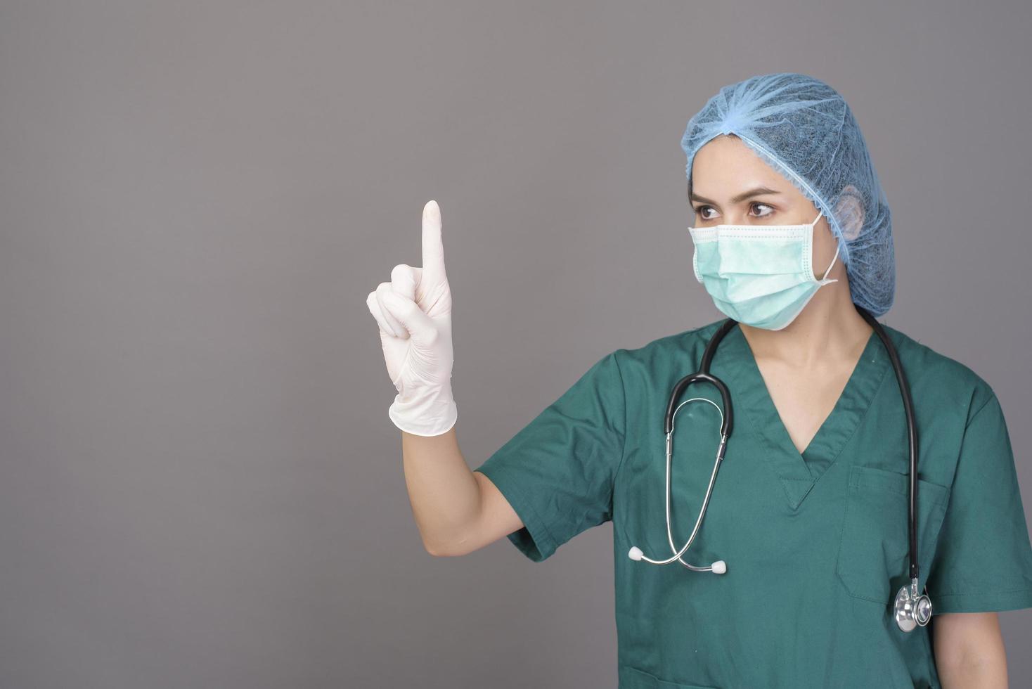 jonge zelfverzekerde vrouw arts in groene scrubs draagt chirurgisch masker over grijze achtergrond studio foto