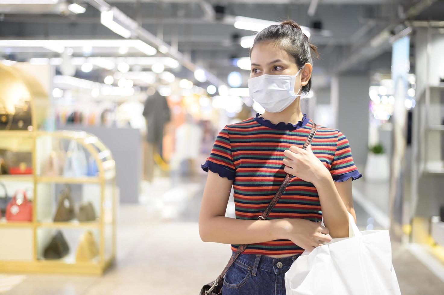 een jonge vrouw die een gezichtsmasker draagt dat in winkelcentrum winkelt. foto