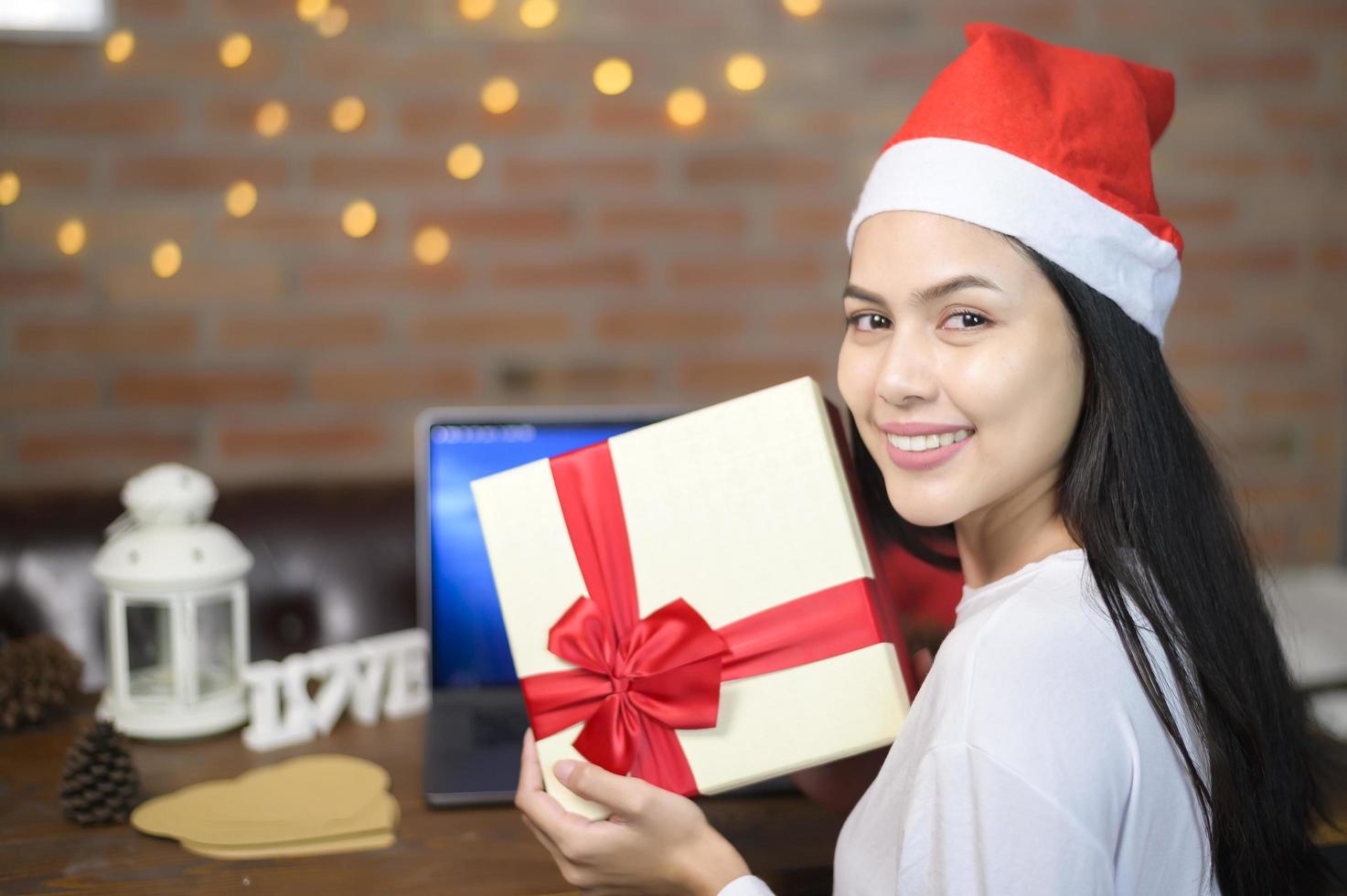 jonge lachende vrouw met rode kerstman hoed video bellen op sociaal netwerk met familie en vrienden op eerste kerstdag. foto