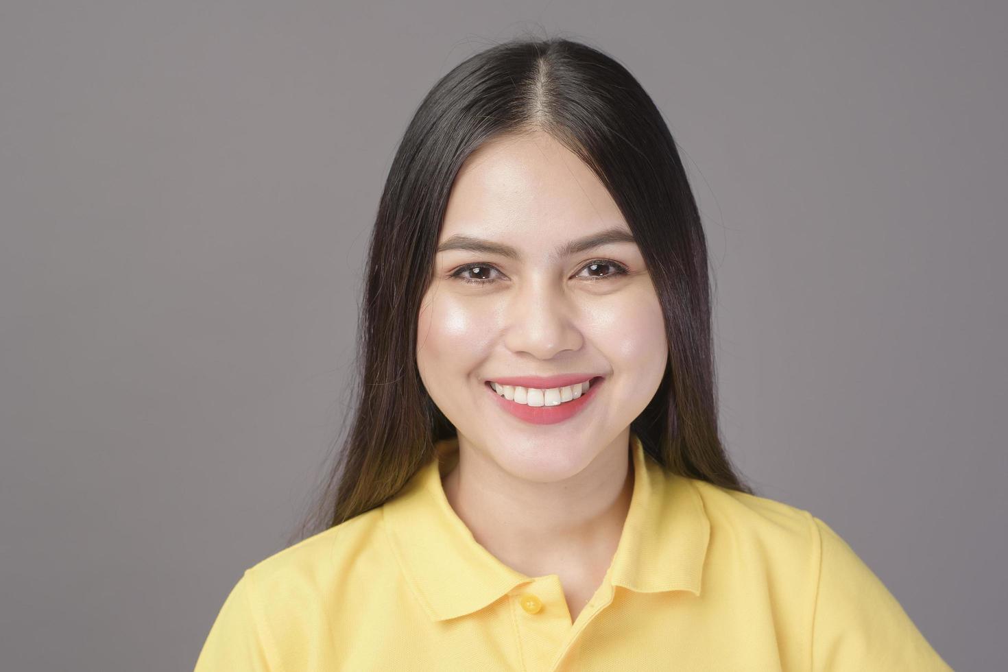 jonge zelfverzekerde mooie vrouw die een geel shirt draagt, staat op een grijze achtergrondstudio foto