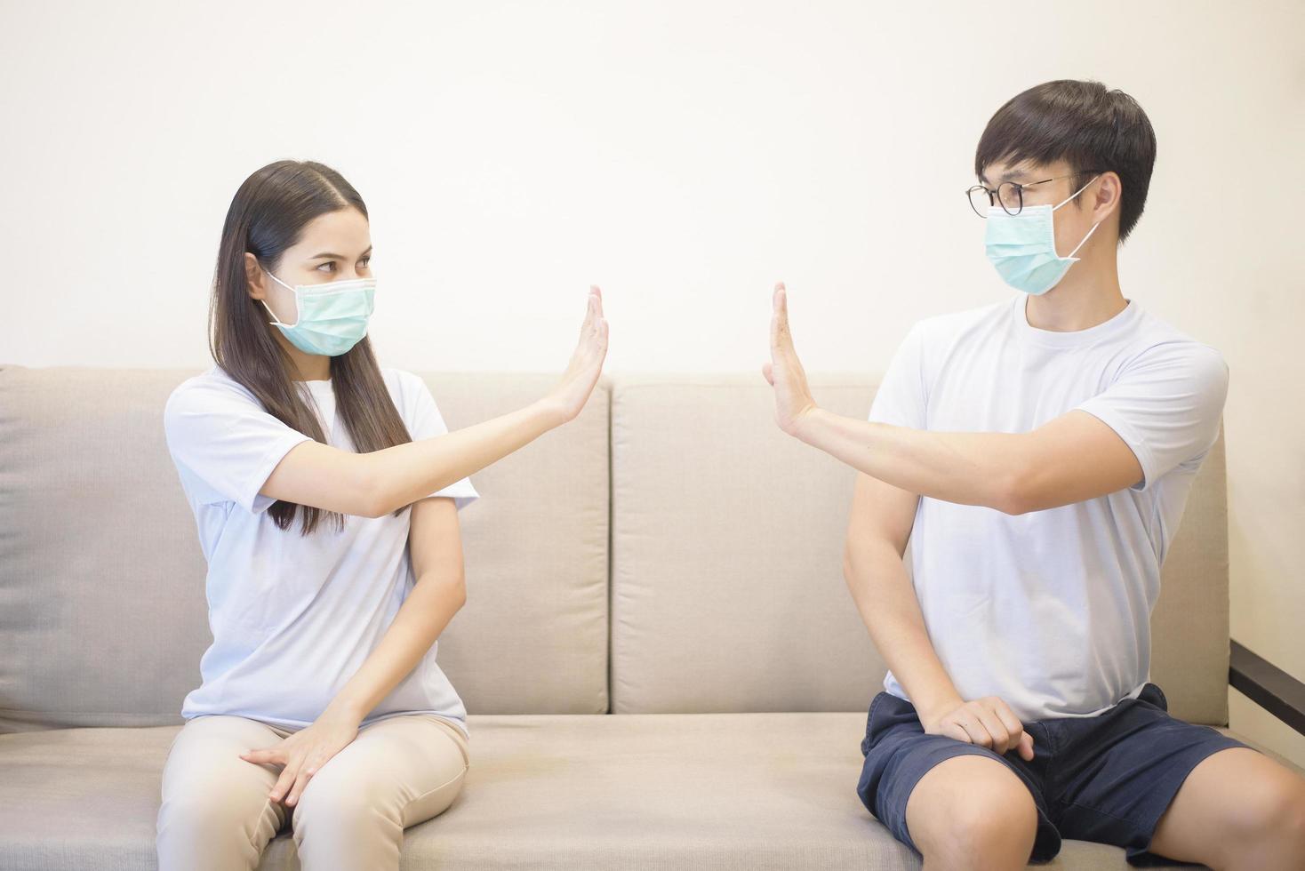 een stel dat een masker draagt, zit thuis op een bank tijdens quarantaine voor bescherming en ter voorkoming van coronavirus foto