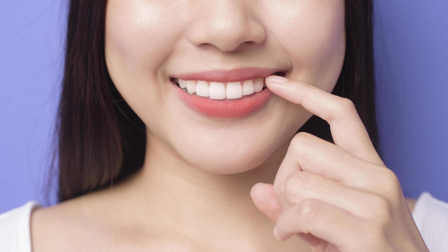 jonge lachende mooie vrouw toont en wijst haar gezonde rechte witte tanden over paarse achtergrond studio foto