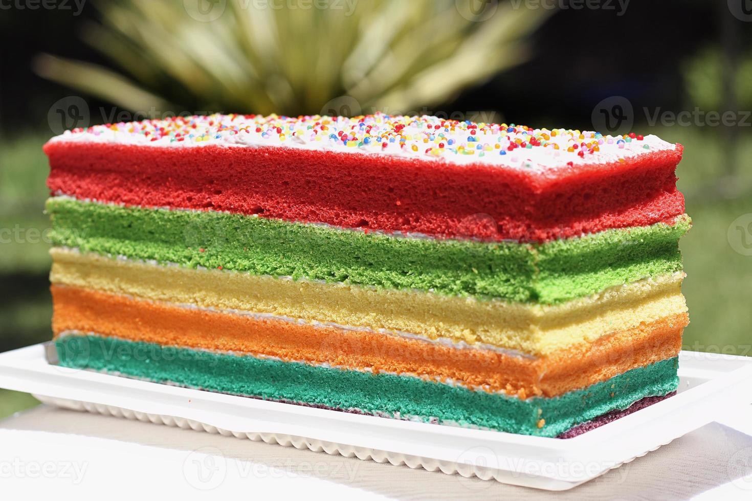 verjaardagsachtergrond - gestreepte regenboogcake met wit glazuur foto