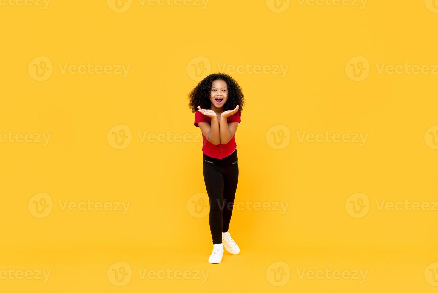 gemengd ras afro meisje in verrast opgewonden gebaar met open handen geïsoleerd op gele achtergrond foto