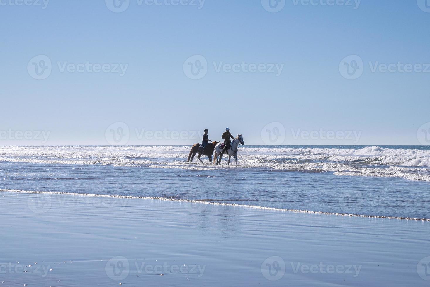 man en vrouw die paarden berijden langs de kustlijn op het strand tegen heldere hemel foto