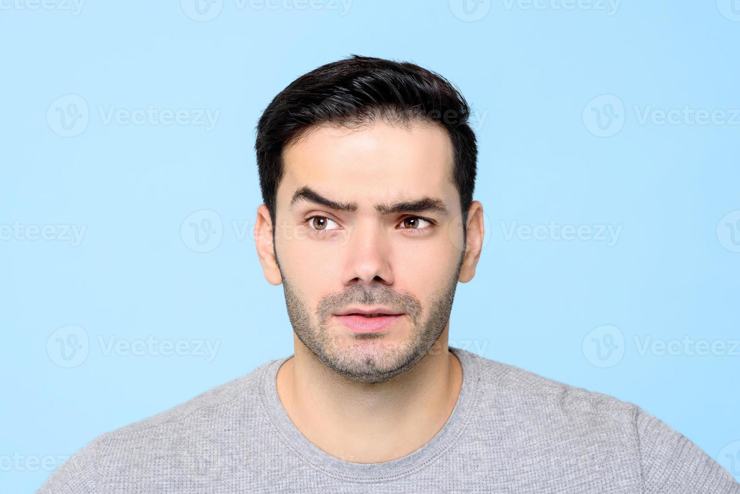 doordachte nieuwsgierige jonge man gezicht met opgetrokken wenkbrauw geïsoleerd op lichtblauwe achtergrondkleur foto