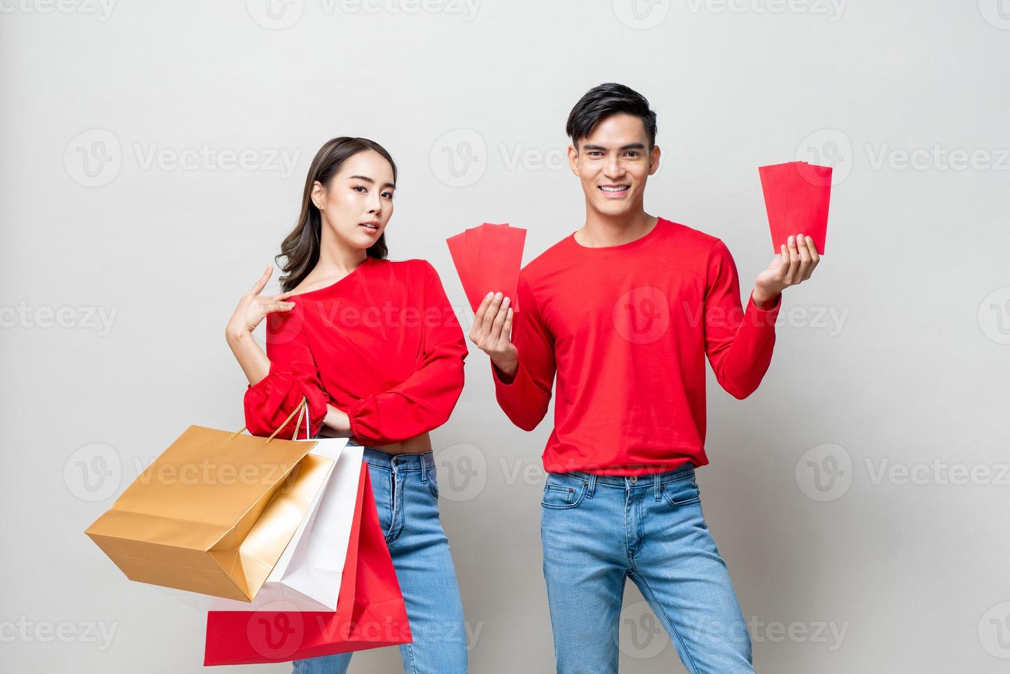 Gelukkig Aziatisch paar met boodschappentassen en rode enveloppen geïsoleerd in grijze studio achtergrond voor Chinees Nieuwjaar verkoop concept foto