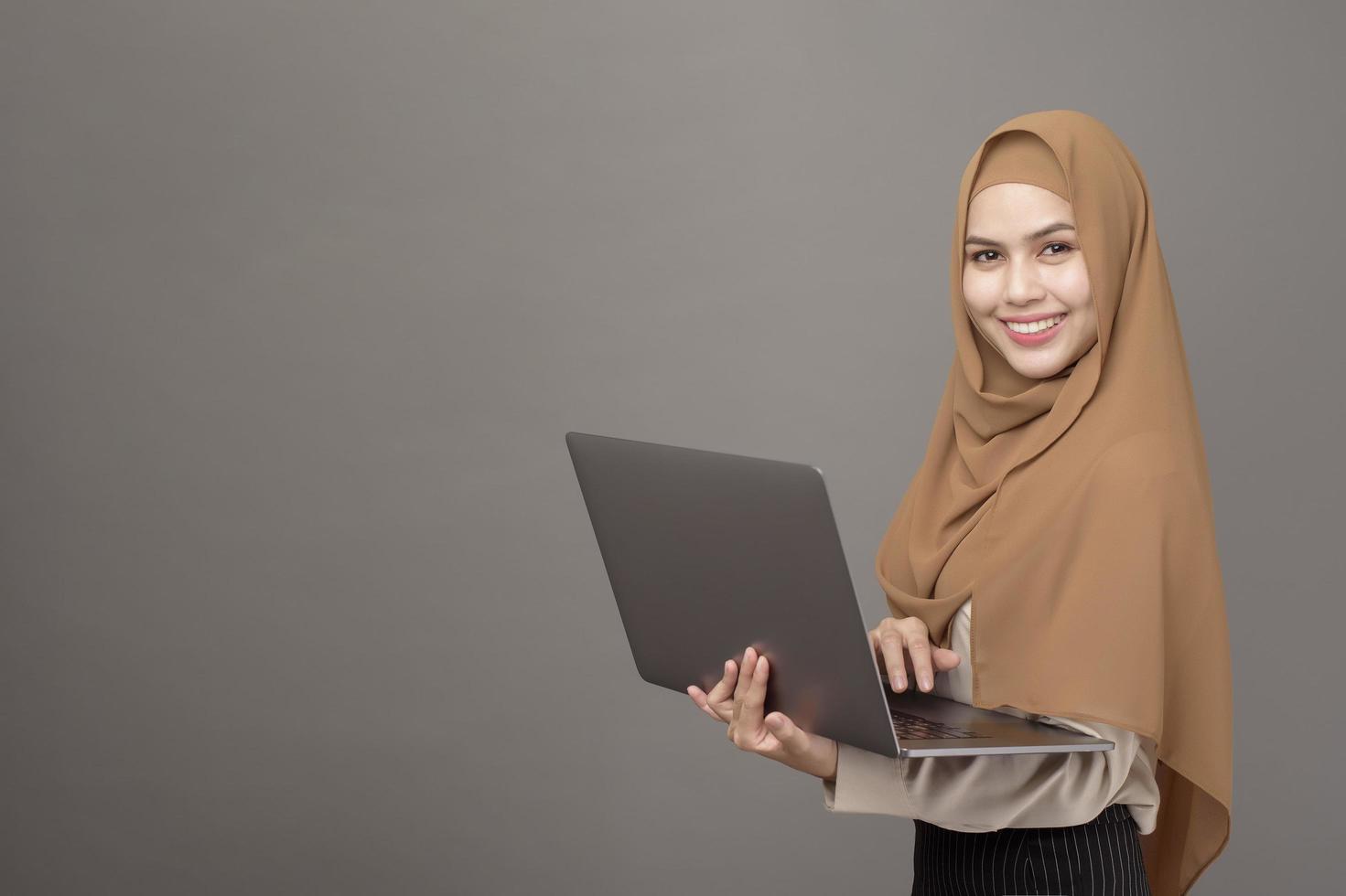 portret van mooie vrouw met hijab houdt computerlaptop op grijze achtergrond foto