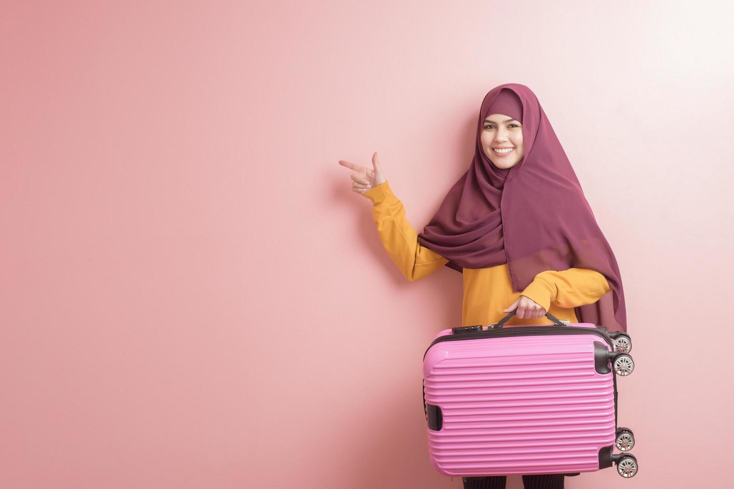 moslimvrouw met hijab houdt bagage op roze achtergrond, mensen reizen concept foto