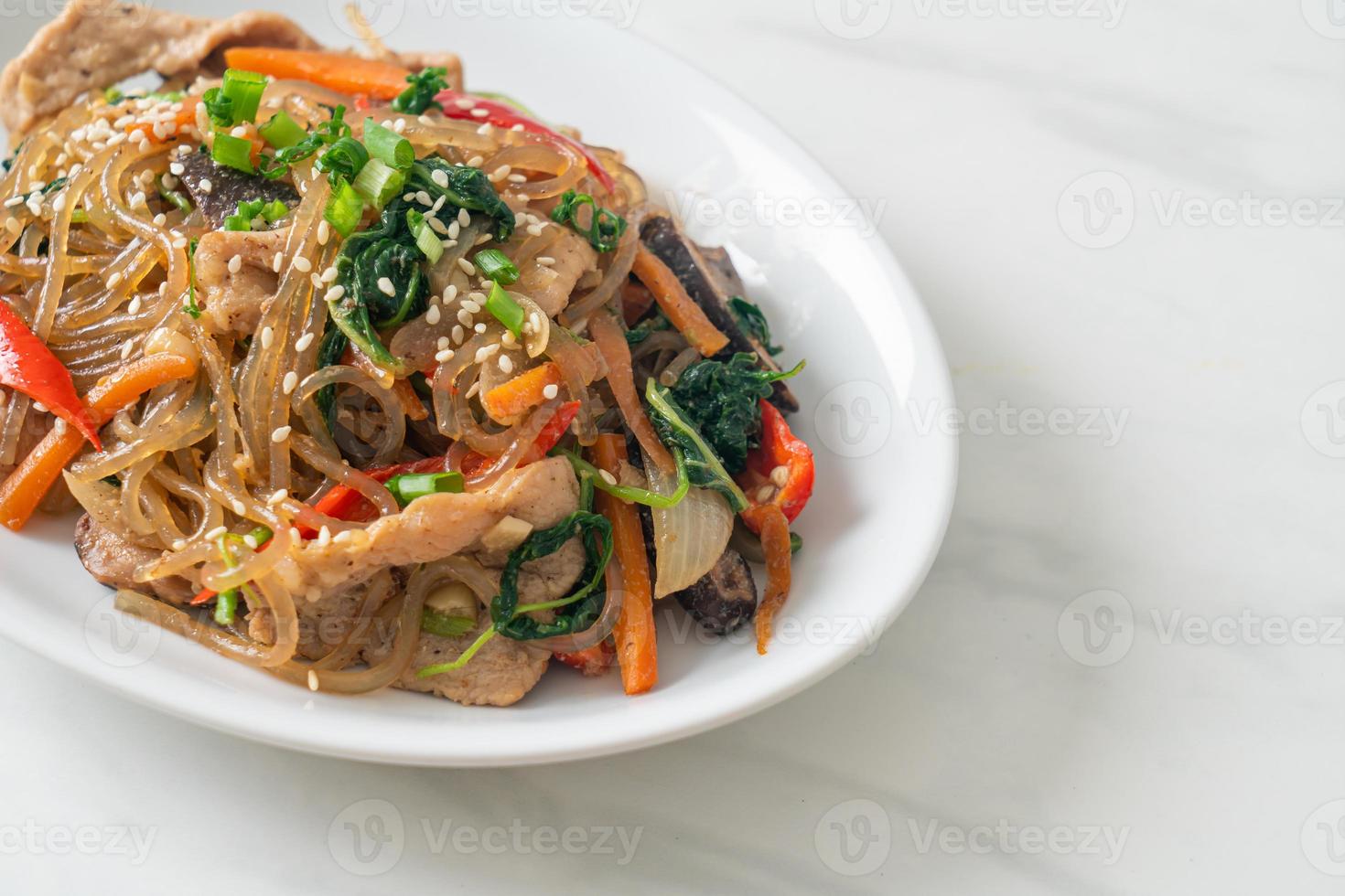 japchae of geroerbakte Koreaanse vermicelli noedels met groenten en varkensvlees gegarneerd met witte sesam foto