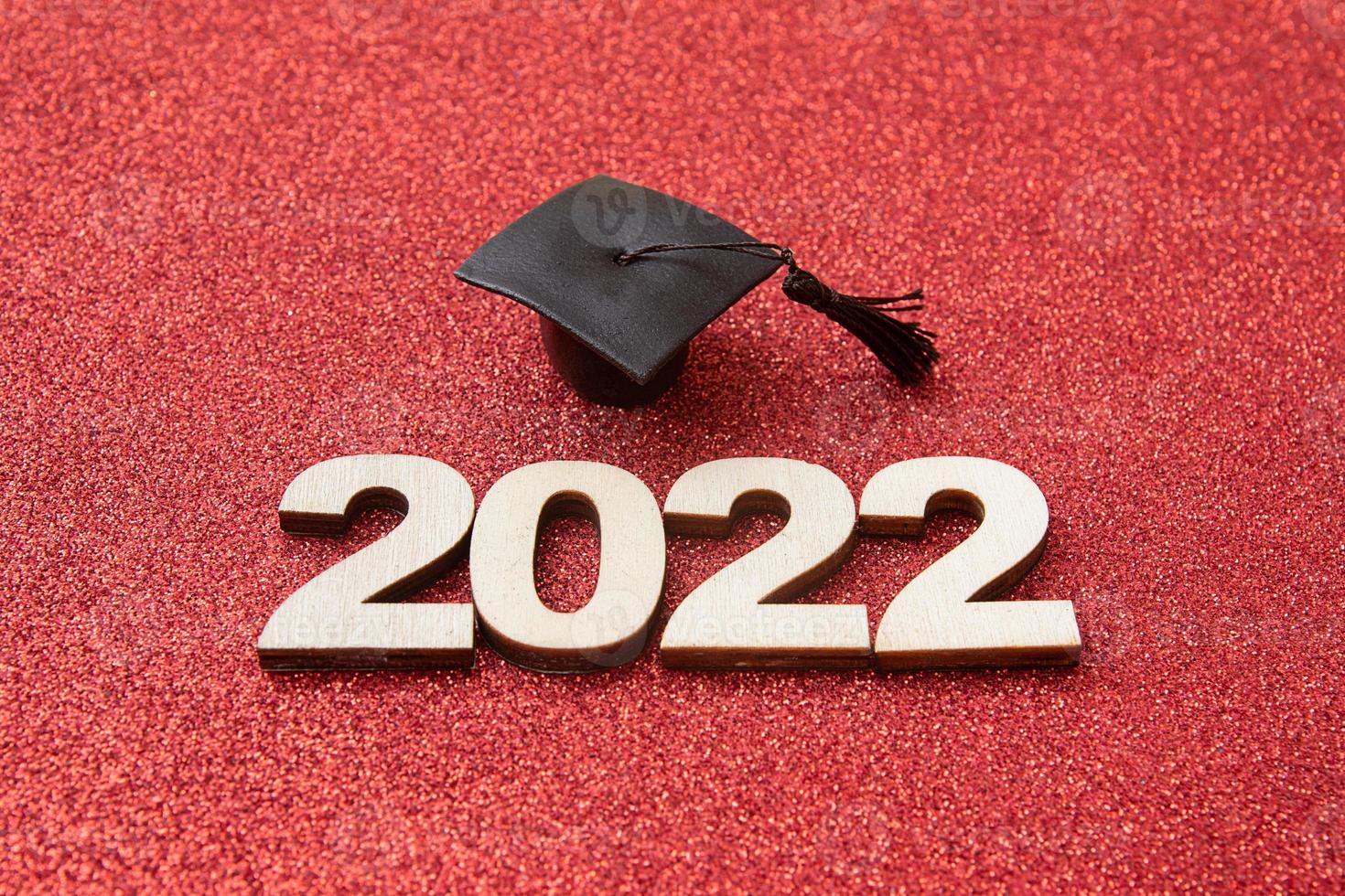 afstudeerhoed met houten nummer 2022 op rode glinsterende achtergrond. onderwijs, leunend, klasse 2022 concept foto