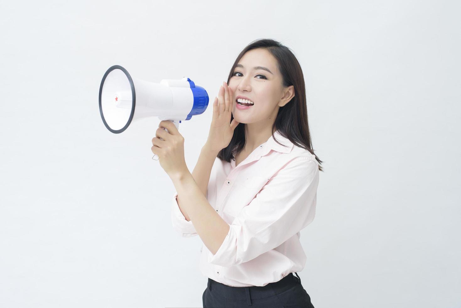 een jonge mooie Aziatische vrouw kondigt door megafoon op witte achtergrond aan foto