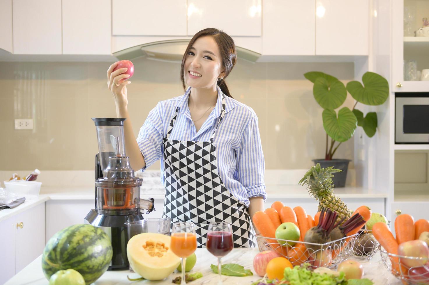 een mooie vrouw bereidt gezond vers sap, terwijl groenten en sapcentrifuges op tafel in de keuken, gezondheidsconcept foto