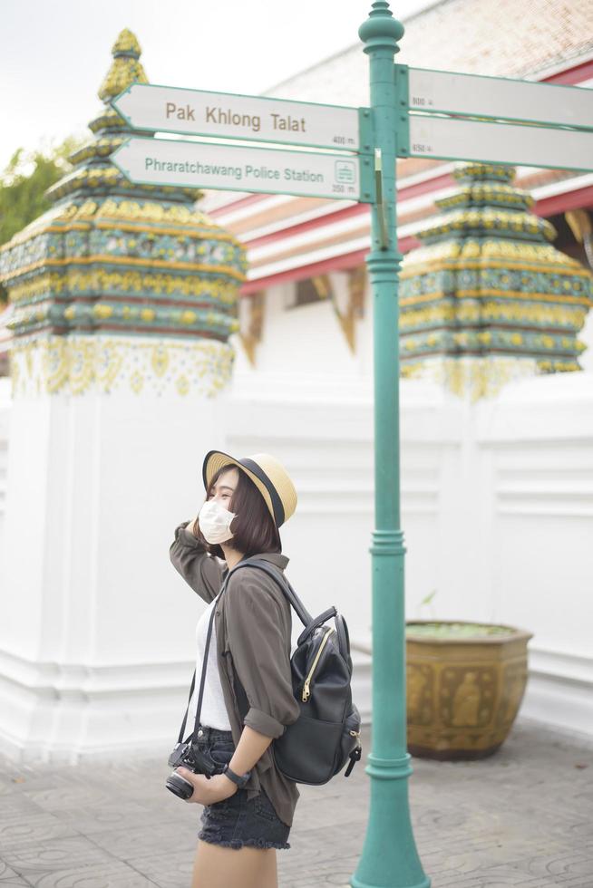 een jonge, mooie aziatische vrouw draagt een beschermend masker dat rond beroemde plaatsen in de stad Bangkok reist, nieuw normaal reizen, covid-19-bescherming, veilige reizen foto