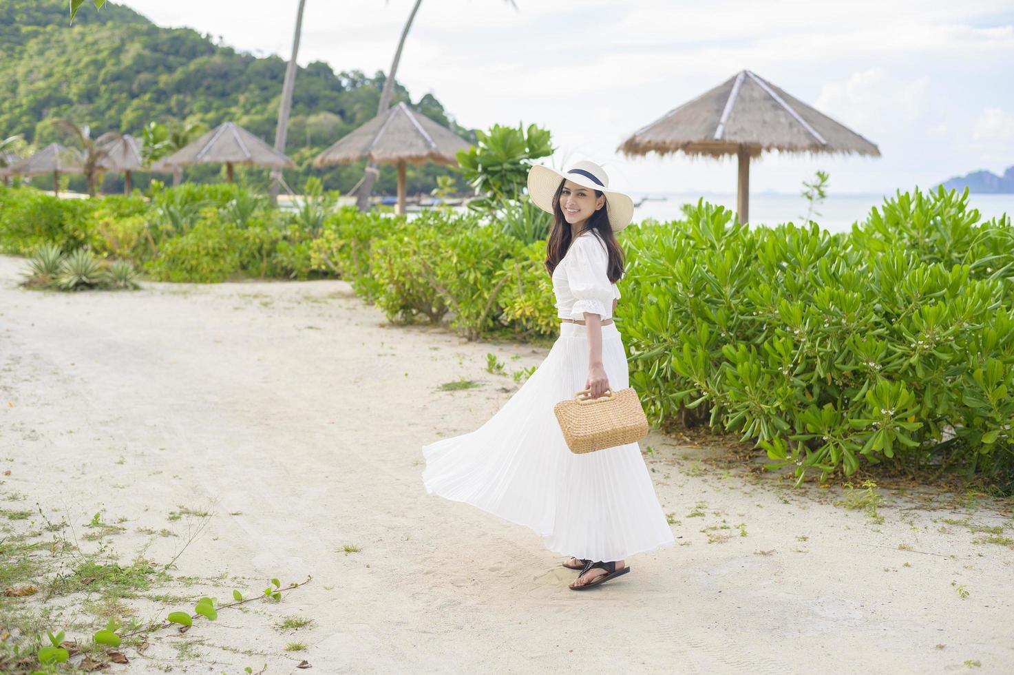 een gelukkige mooie vrouw in een witte jurk die geniet en ontspant op het strand, zomer en vakantie concept foto