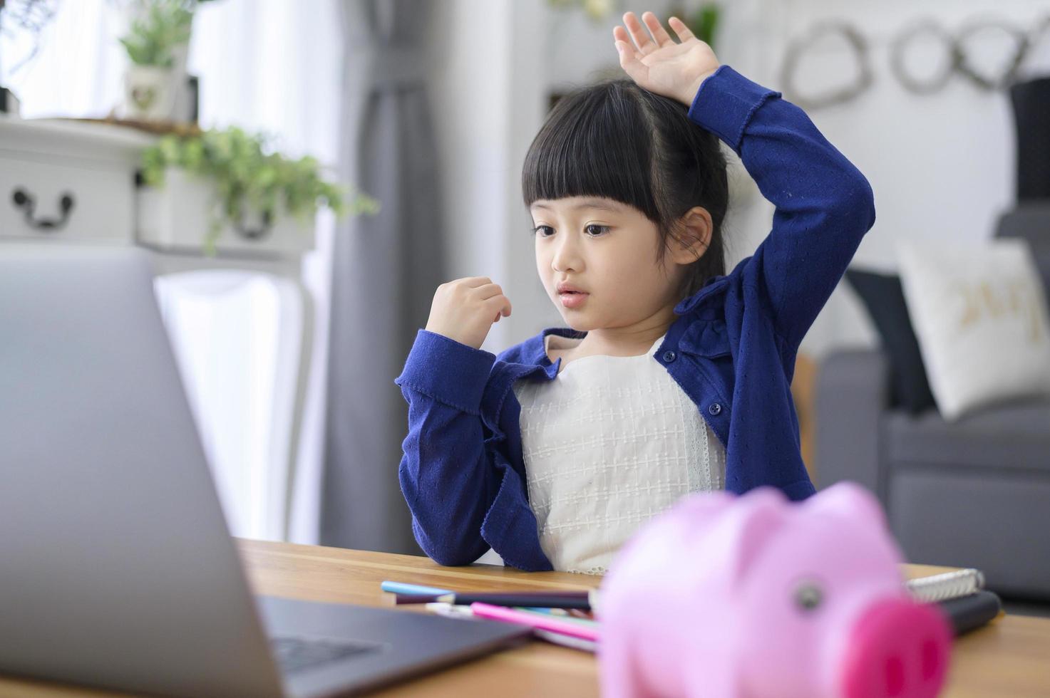 een klein schattig meisje gebruikt een laptop om thuis online via internet te studeren. e-learningconcept tijdens quarantainetijd. foto