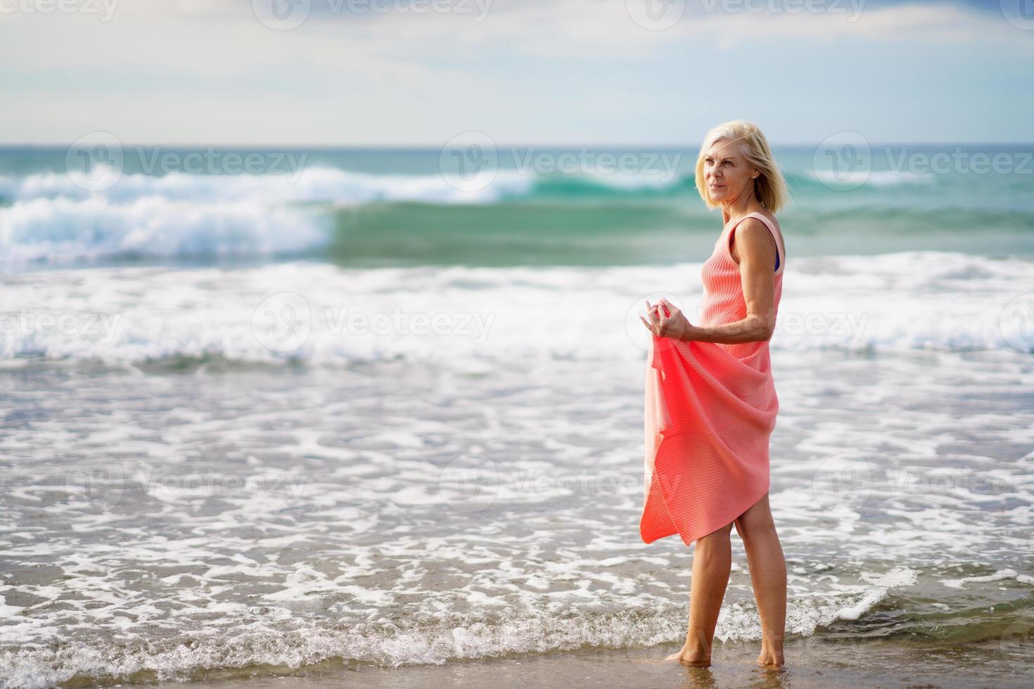 volwassen vrouw geniet van haar vrije tijd kijkend naar de zee vanaf de kust van het strand. foto