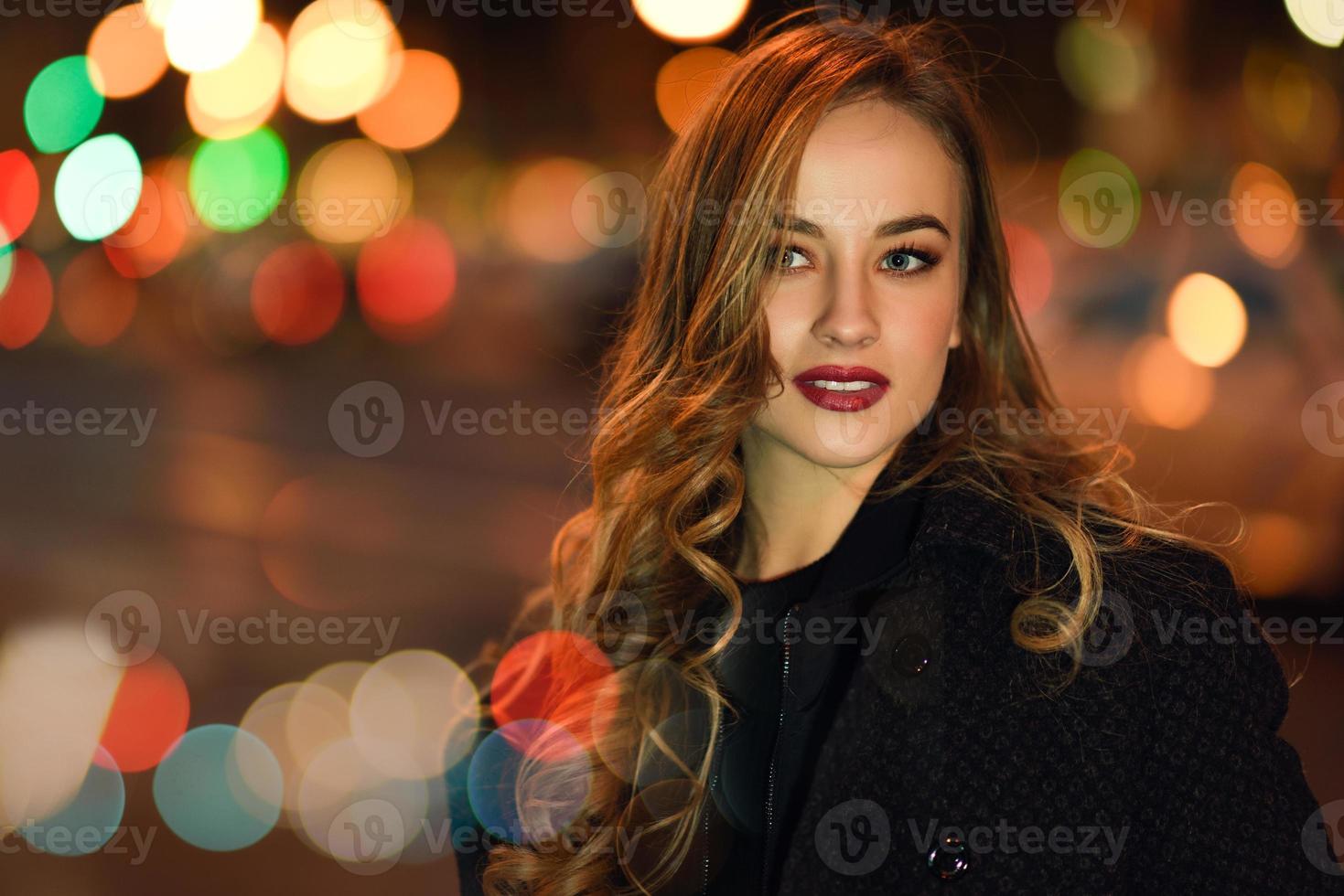 vrouw met zwarte jas op straat met onscherpe lichten foto