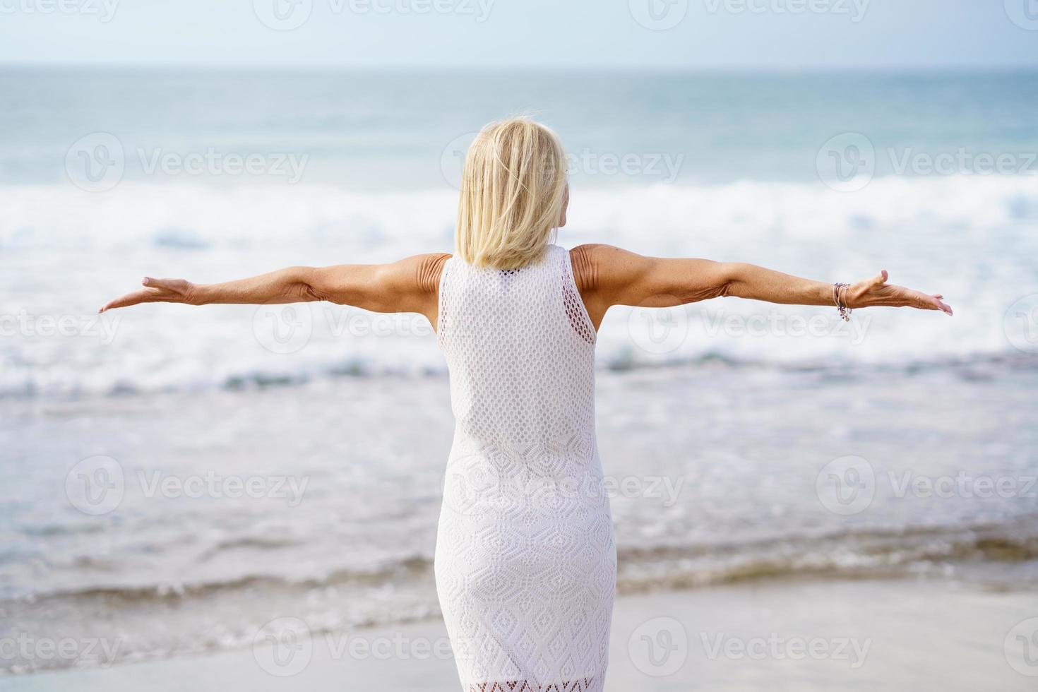 volwassen vrouw die haar armen op het strand opent, haar vrije tijd doorbrengt, geniet van haar vrije tijd foto