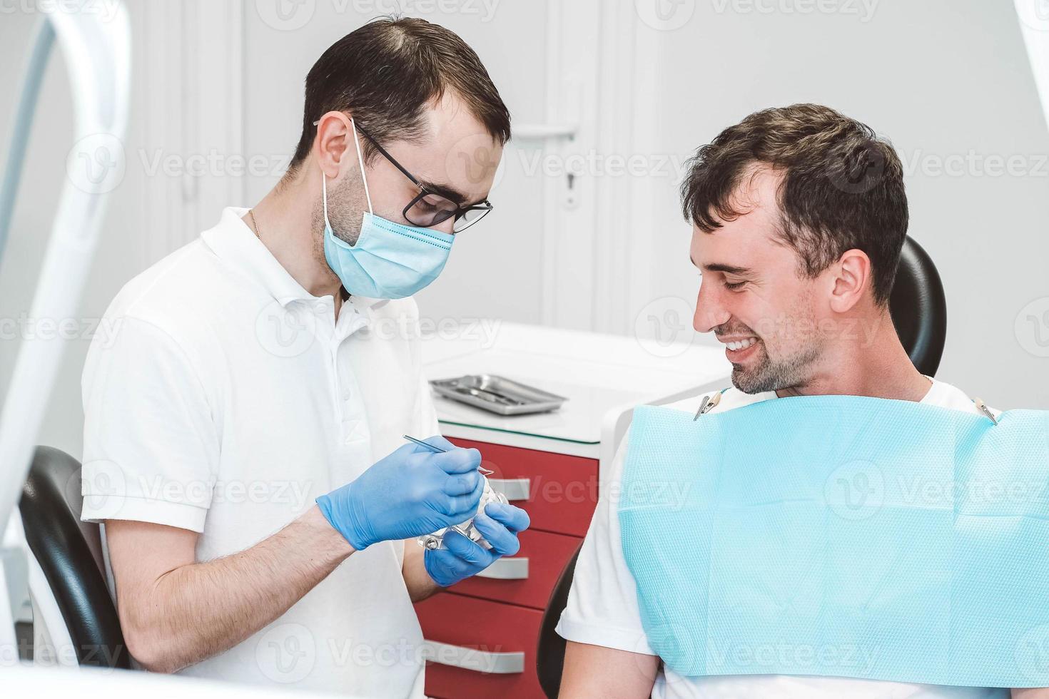 tandarts raadpleegt en praat met de mannelijke patiënt op de tandartsstoel foto