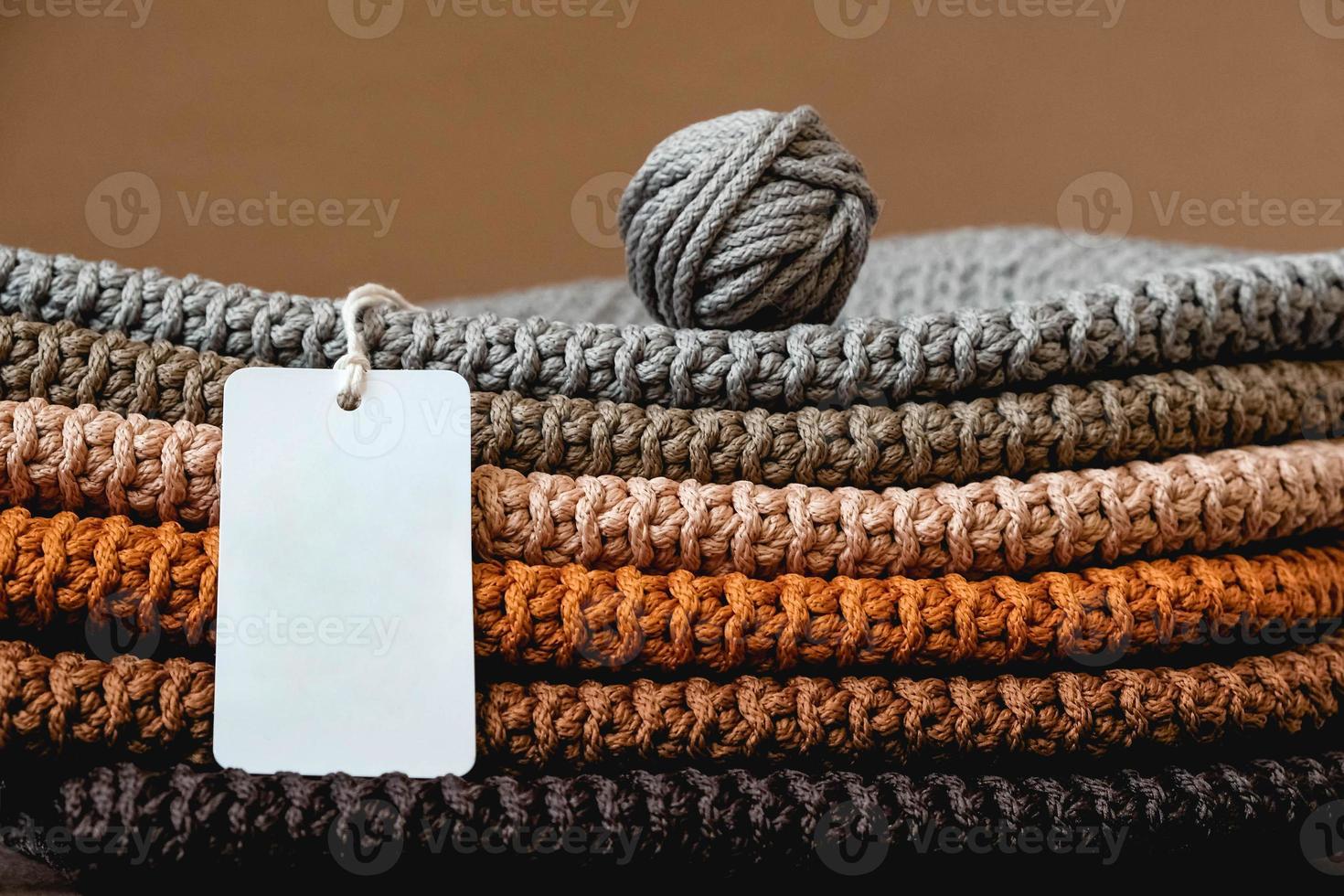 stapel gebreid materiaal van draden van bruine, oranje, grijze kleuren met een leeg prijskaartje op een bruine achtergrond foto