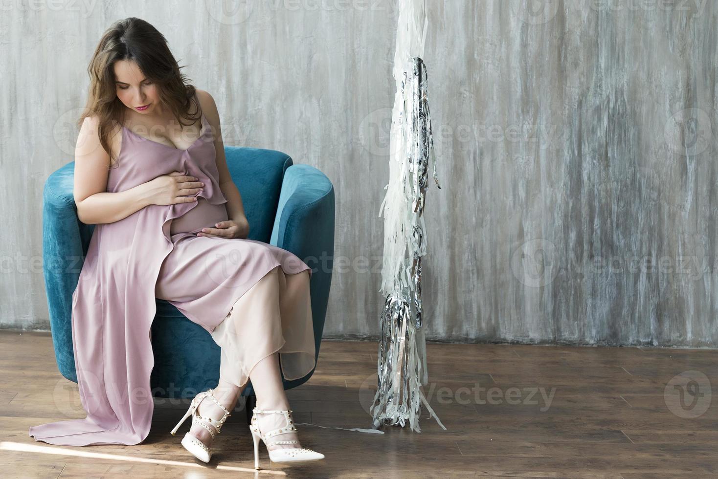 een jonge zwangere vrouw in een paarse jurk zittend op een stoel. foto