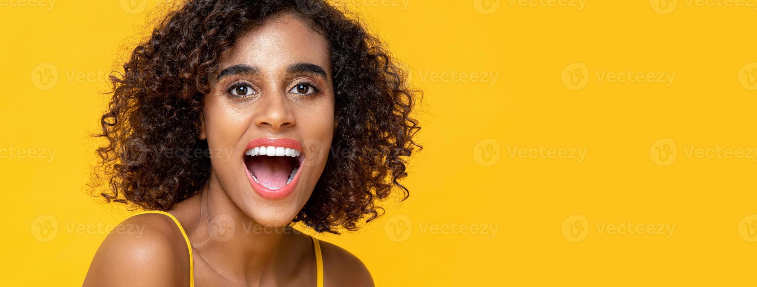 close-up portret van een gelukkige Afro-Amerikaanse vrouw die naar de camera kijkt met open mond in een geïsoleerde studio gele bannerachtergrond foto