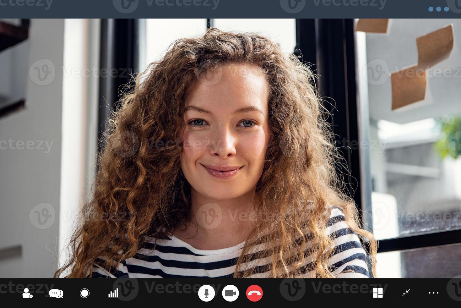 gelukkige, mooie blanke vrouw die naar de camera lacht terwijl ze thuis een videogesprek voert foto