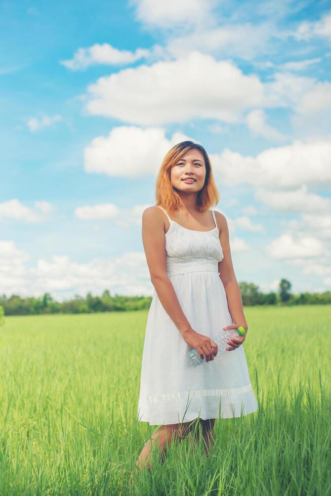 vrouwen levensstijl concept jonge mooie vrouw, gekleed in witte jurk met fles water op grasland smiley naar camera kijken zo fris genieten en gelukkig. foto