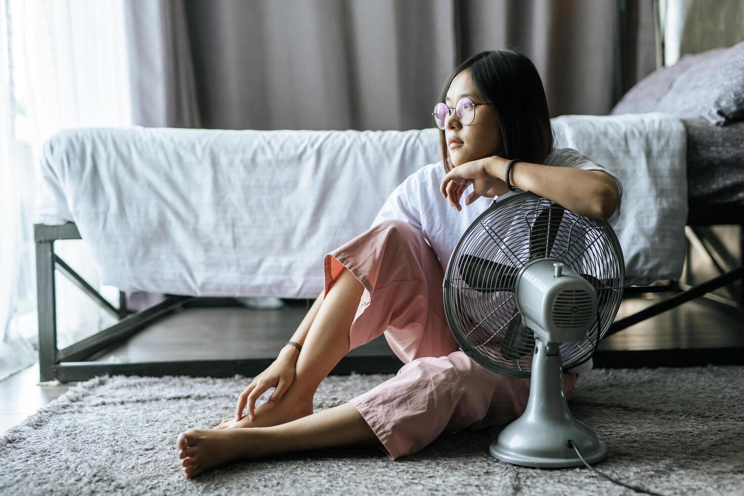 de vrouw droeg een wit overhemd en hand, ging bij de tafelventilator zitten en keek naar buiten. foto