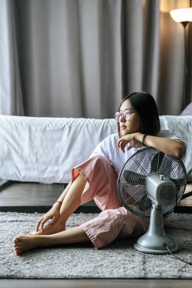 de vrouw droeg een wit overhemd en hand, ging bij de tafelventilator zitten en keek naar buiten. foto