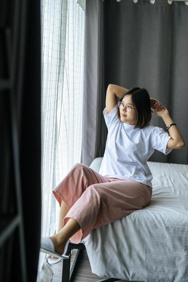 een vrouw in een wit overhemd die op het bed zit en beide armen opheft. foto