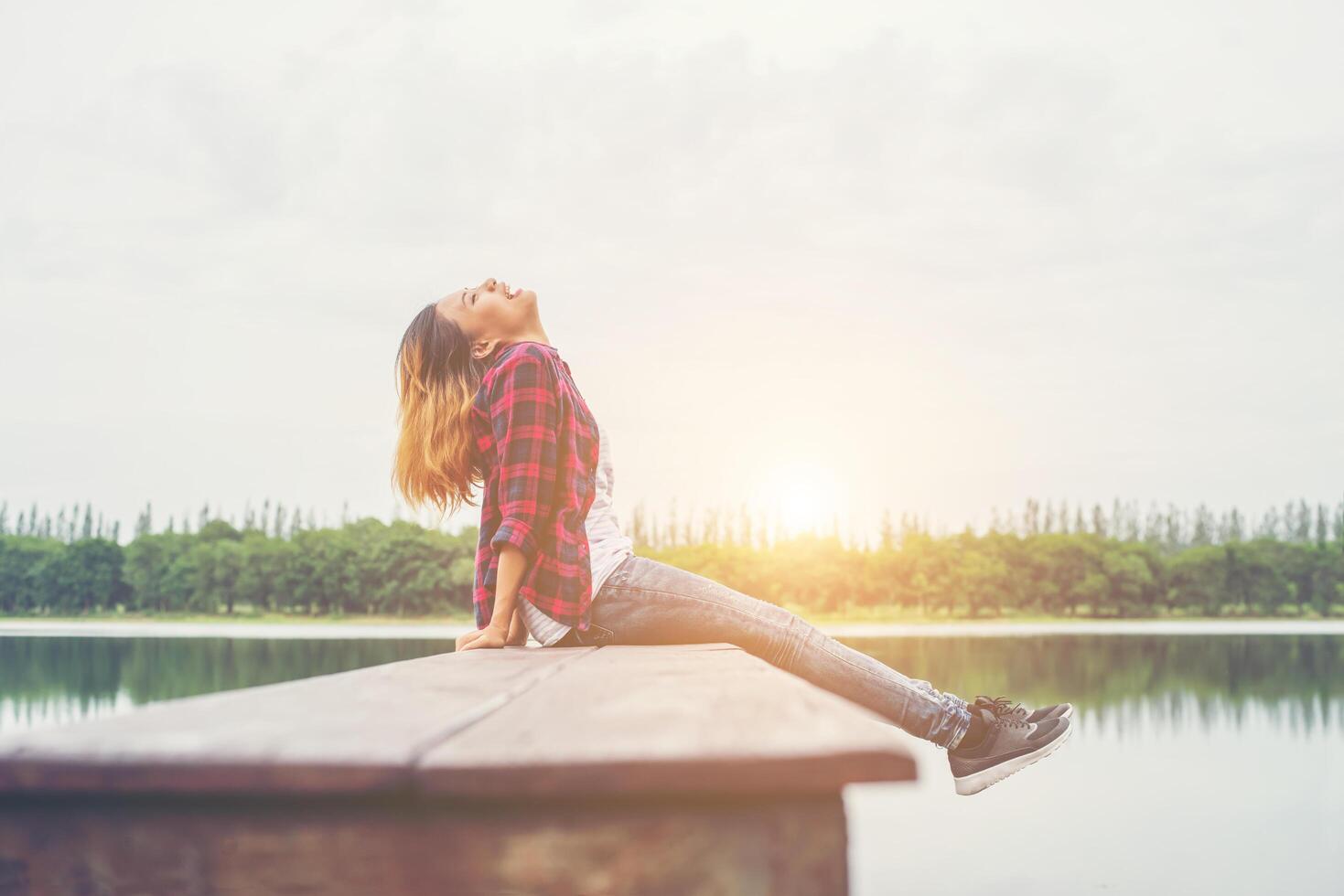 jonge hipster vrouw zittend op een houten pier, ontspannen liggend been naar het meer. foto