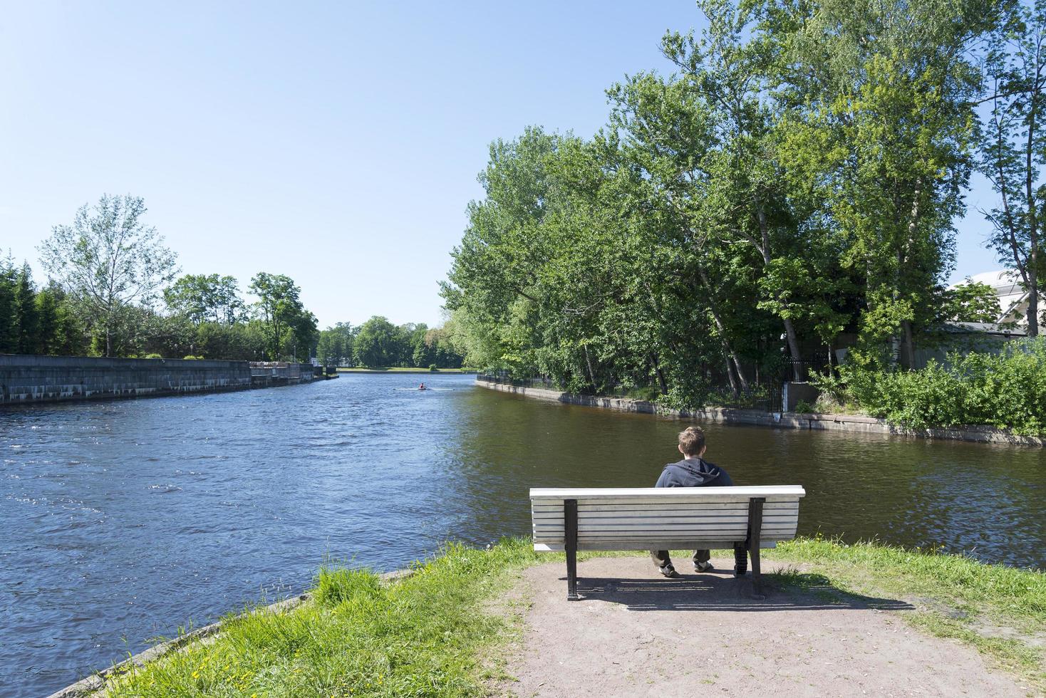 een jonge man zittend op een bankje in de buurt van de rivier. foto