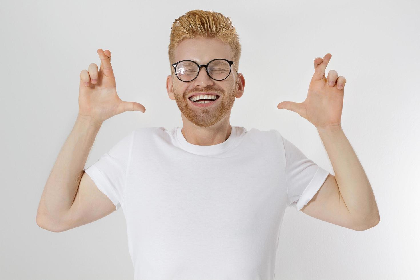 vingers gekruist, maak een wensconcept. jonge roodharige man met rode baard kruisvinger voor geluk. handteken, gebaar voor dromen die uitkomen. gelukkig lachende man in lege sjabloon wit t-shirt. mock-up foto