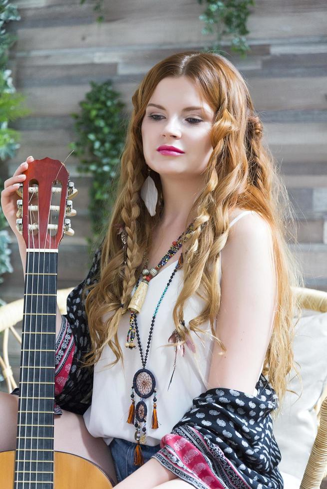 een mooi meisje met rood krullend haar zit op een stoel met een zevensnarige gitaar. foto