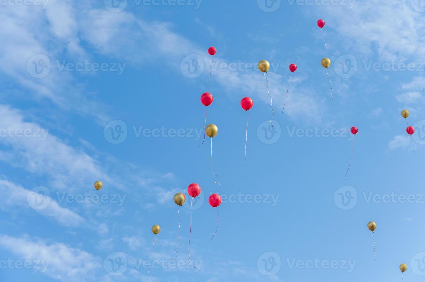 veel rode en gouden ballonnen vliegen onder de blauwe lucht en witte wolken foto