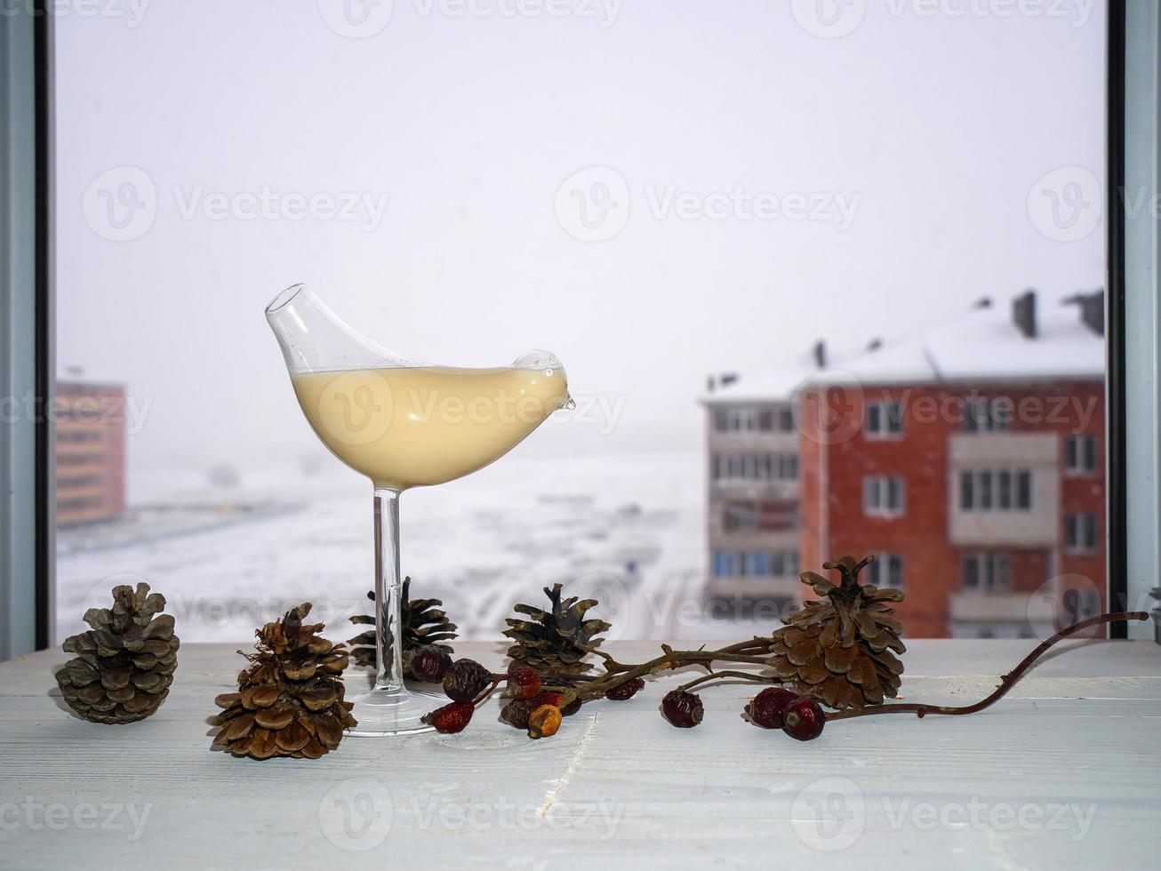 Havermelk in een decoratief glas in de vorm van een vogel op een witte tafel met kegels en rozenbottels. sneeuw op de achtergrond foto