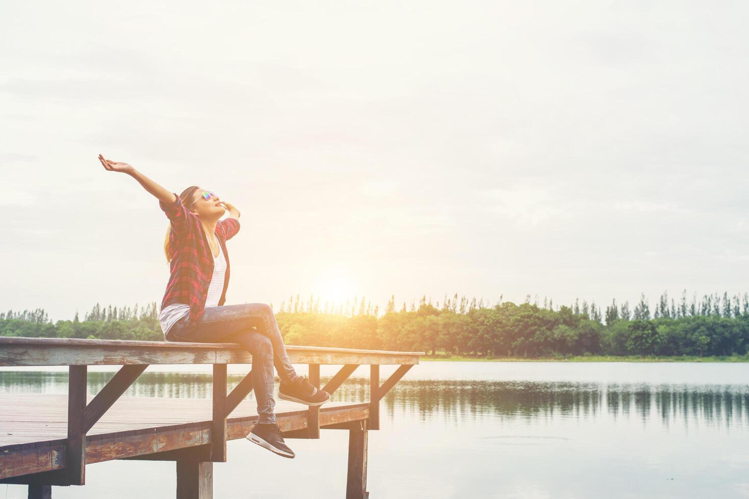 jonge hipster vrouw zittend op de pier opgeheven handen, ontspannen met natuurlijke vrijheid, genieten en gelukkig. foto