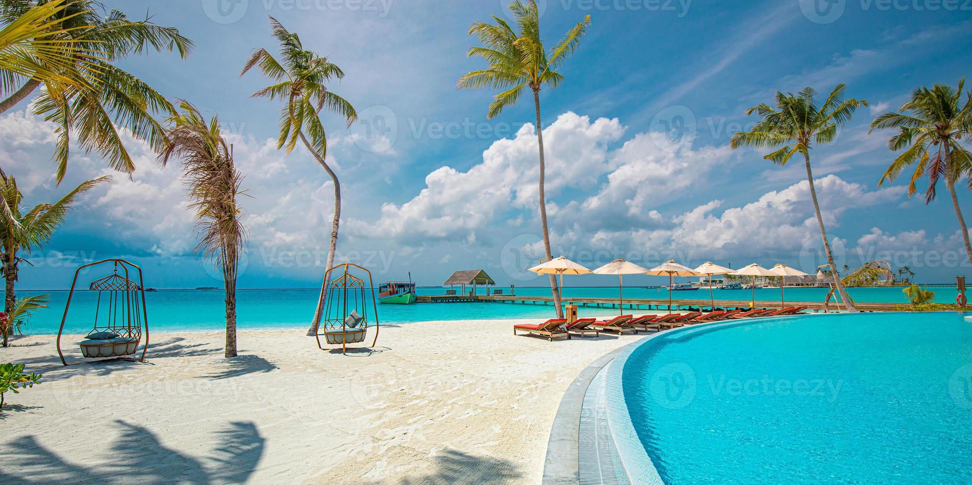 panoramisch vakantielandschap. luxe strandresort hotel zwembad en strandstoelen of ligstoelen onder parasols met palmbomen, blauwe zonnige hemel. zomer eiland aan zee, reizen vakantie achtergrond foto