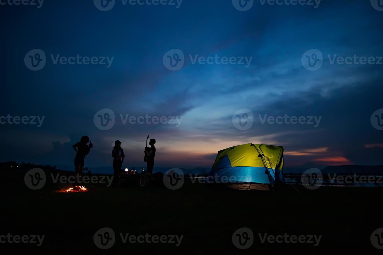 silhouetgroep aziatische vrienden toeristen drinken en spelen gitaar samen met geluk in de zomer terwijl ze kamperen in de buurt van het meer foto